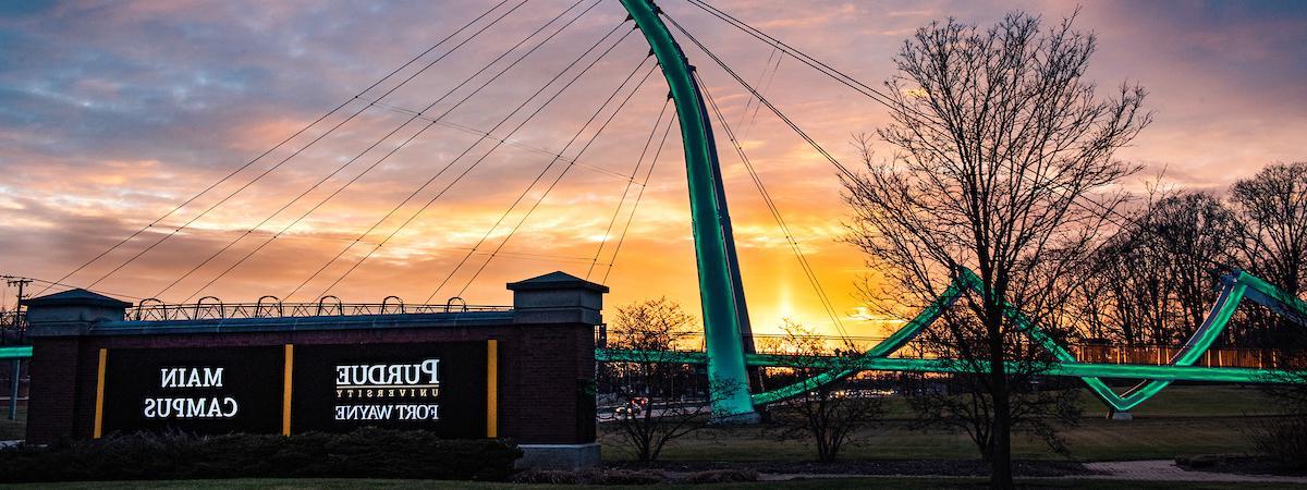 Campus sign with the bridge and a sunrise in the background.